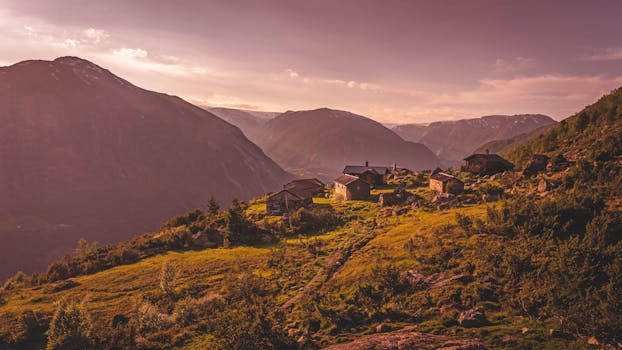 A serene mountain village with wooden cabins nestled on a lush hilltop during dusk.