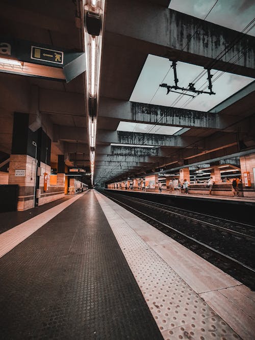 People waiting for transport at platform of railway station with glowing lamps on ceiling