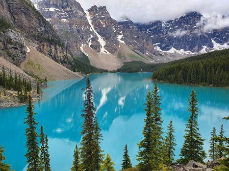 Beautiful view of Moraine Lake surrounded by snow-capped Rocky Mountains and lush pine forests.