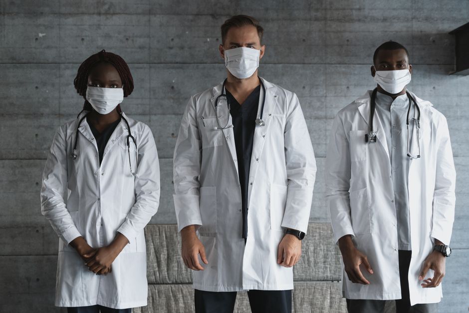A diverse group of doctors in white coats and masks standing indoors, signifying unity in healthcare.
