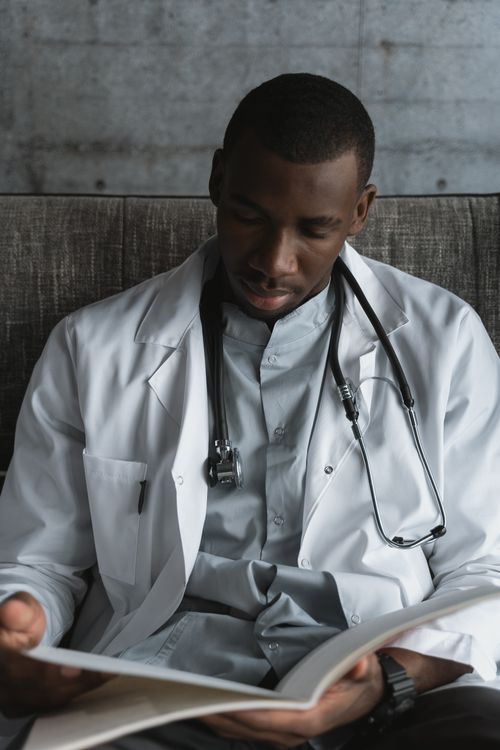Free A focused young doctor in a white coat reading a book indoors. Stock Photo