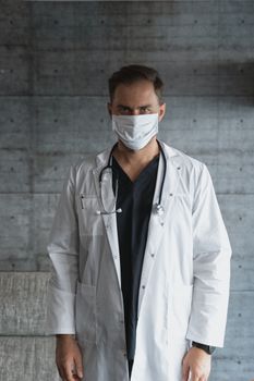 医疗专业人士戴着口罩、穿着实验服，靠在灰色的墙上