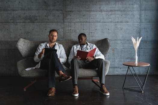 Two doctors in a modern office, reviewing patient files on a sofa.