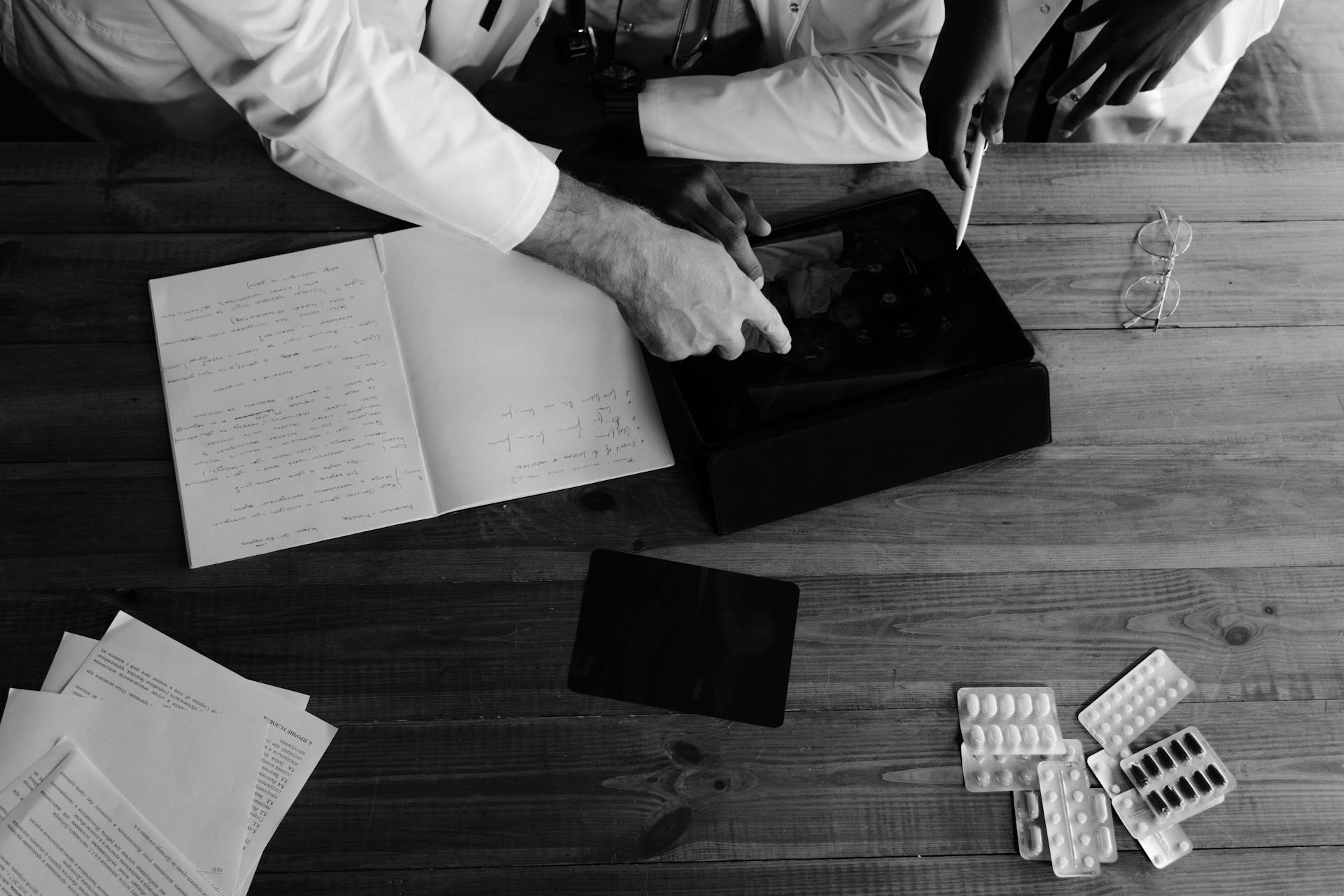 Doctors collaborating on medical research using tablets and notebooks in a monochrome setting.