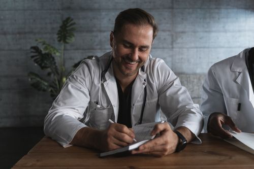 Free A smiling doctor taking notes in a medical office setting. Stock Photo