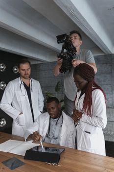 A group of medical professionals collaborating on a project while being recorded by a cameraman.