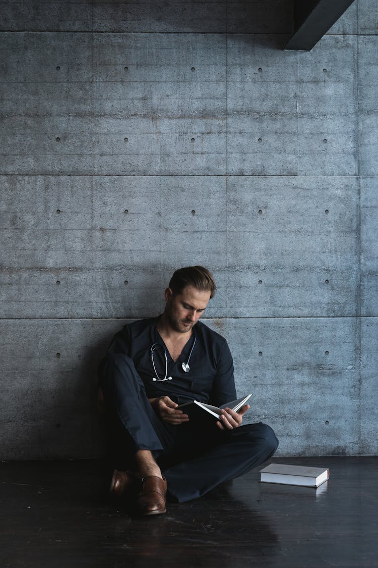 Focused Doctor Reading A Book While Sitting On A Floor 