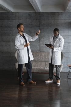Two male doctors in lab coats reviewing medical information on a tablet indoors.