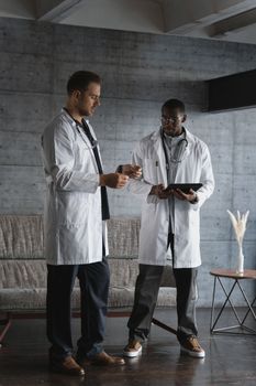 Two doctors in white lab coats examine medical data on a tablet indoors.