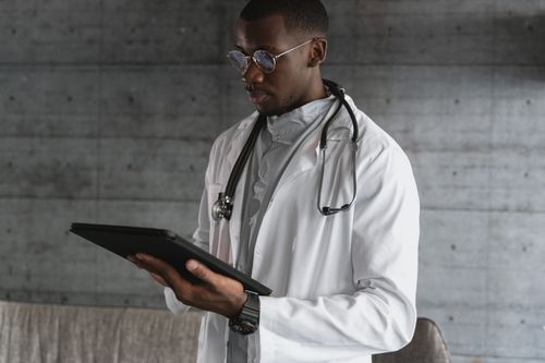 Free A healthcare professional using a tablet indoors, wearing a white coat and stethoscope. Stock Photo