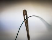 Detailed shot of a sewing needle with thread, highlighting precision and craftsmanship.