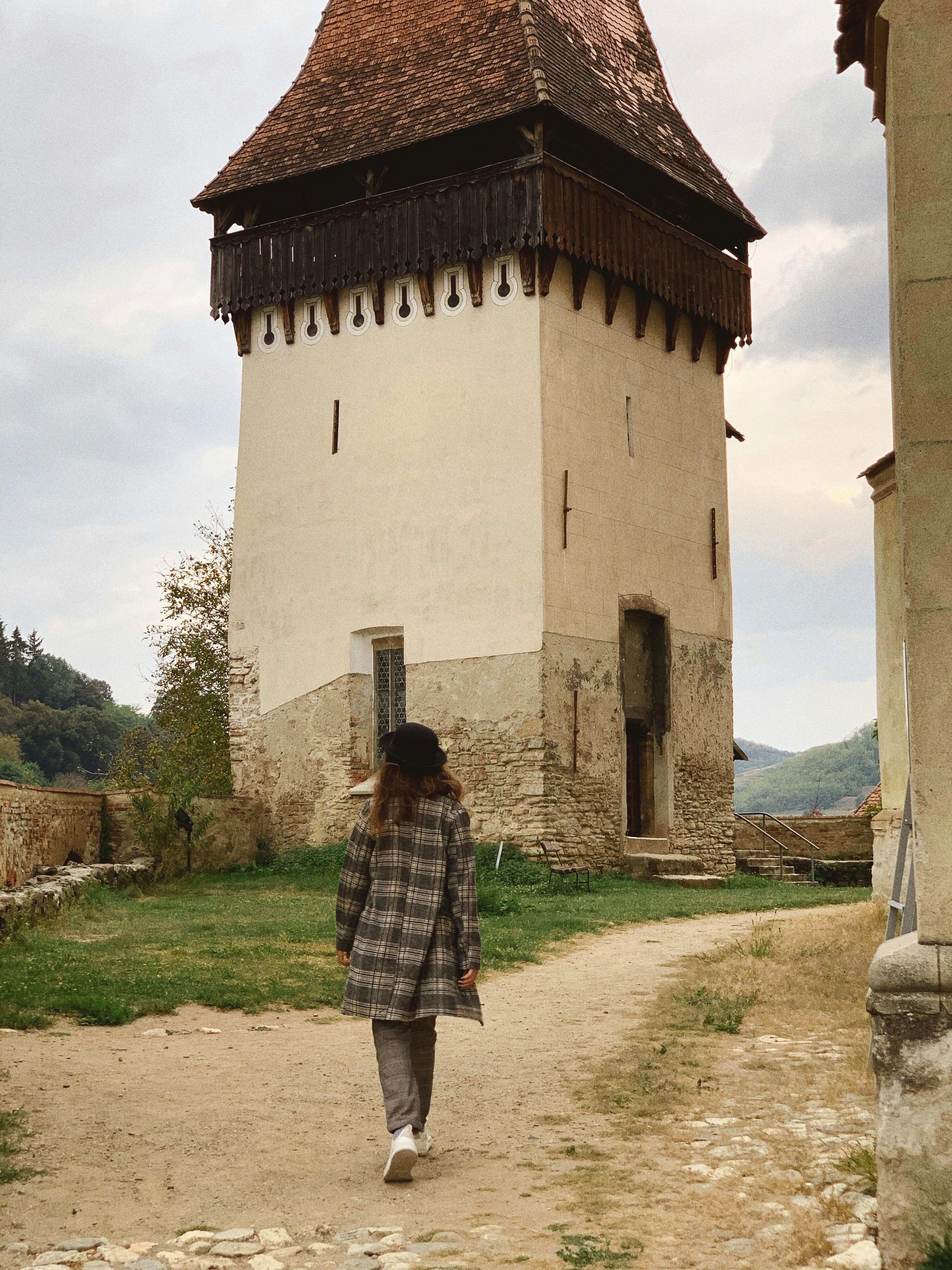 Back view of anonymous female tourist walking along path towards ancient Biertan fortified church against cloudy sunset sky in Romania
