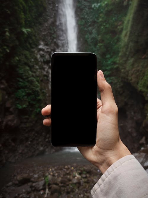 Crop anonymous tourist using smartphone while exploring ravine with rapid waterfall during trip in exotic nature