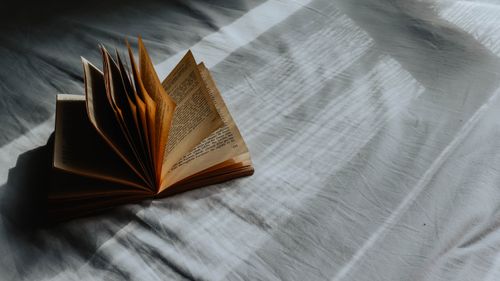 Free An open book lays on a bed, capturing light and shadow play in a cozy indoor setting. Stock Photo
