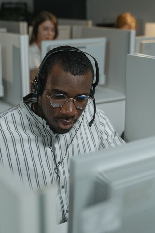 Free Customer support representative wearing glasses and headset in a busy call center setting. Stock Photo