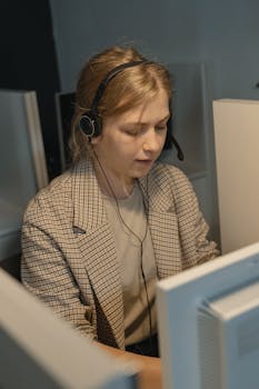 Close-up of a woman in a call center wearing a headset and plaid blazer, focused on work.