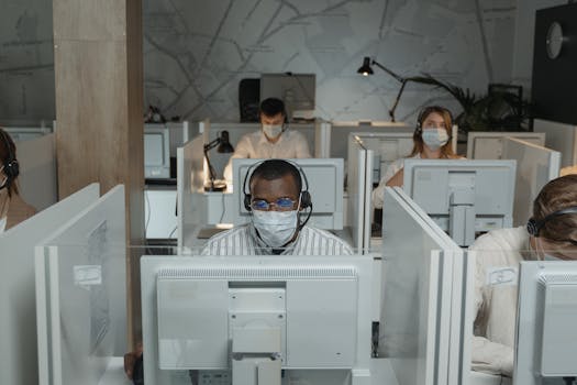 Call center agents wearing face masks working at individual stations in an office.