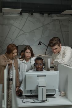 Diverse team of young professionals collaborating around a computer in a modern office setting.