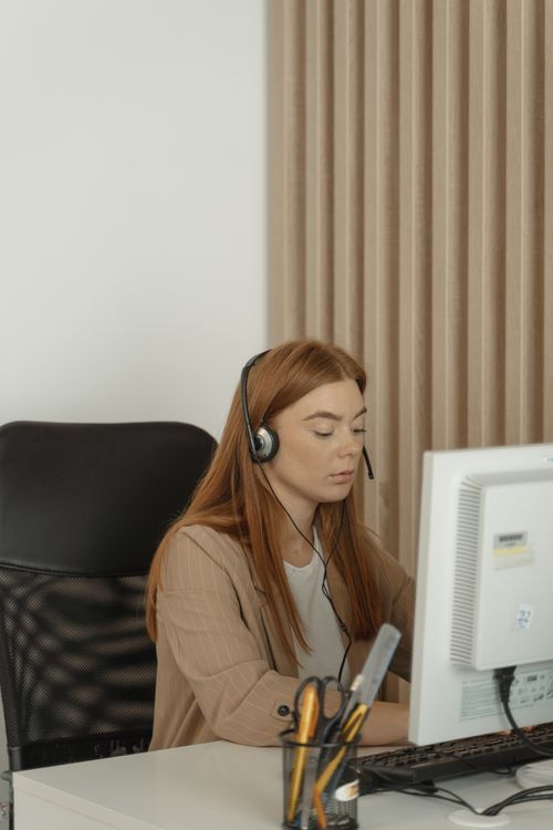 Free Focused woman in an office setting working with a desktop computer and headset. Stock Photo