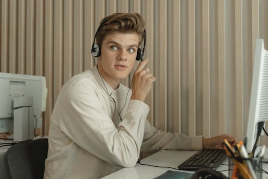 Young man sitting at a desk with headphones, working in a professional office environment.