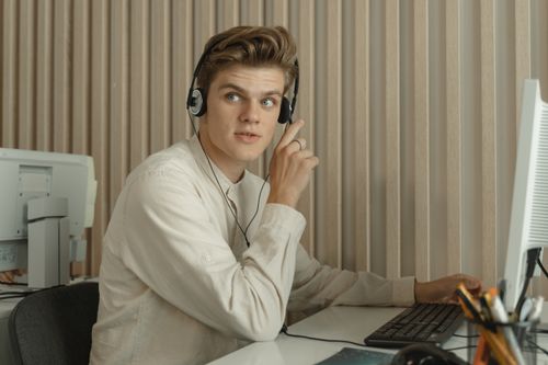 Free Young man sitting at a desk with headphones, working in a professional office environment. Stock Photo