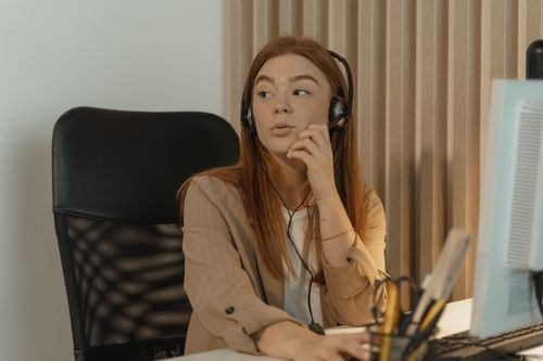 Free Young woman seated at a desk talking with a headset in a modern office environment. Stock Photo