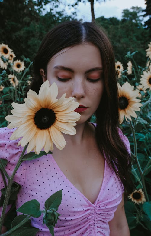 Young female in casual wearing looking down in filed of fresh blooming flowers with green leaves