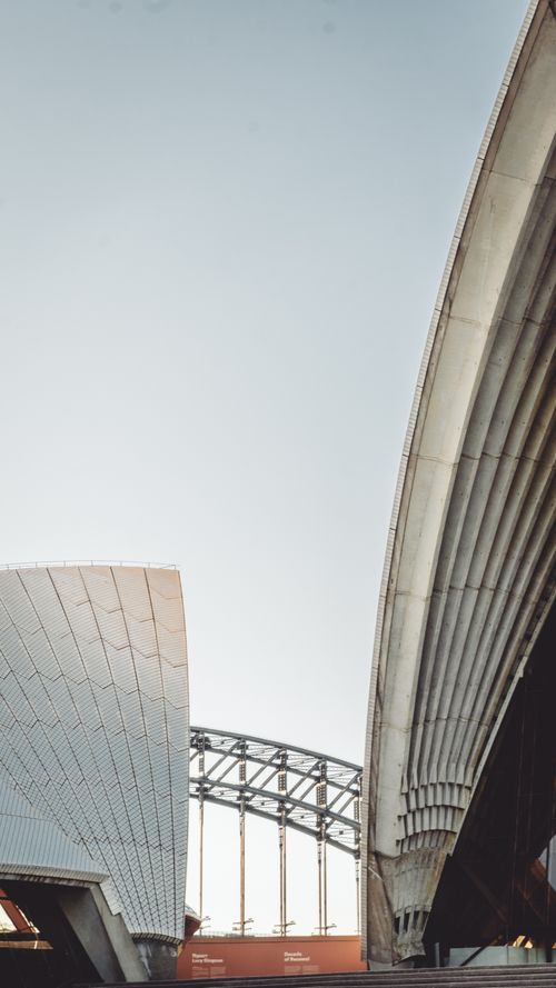 Free Dramatic perspective of the Sydney Opera House and Harbour Bridge, showcasing iconic architecture against a clear sky. Stock Photo