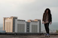 年轻的滑板运动员坐在屋顶上，背景是现代城市景观