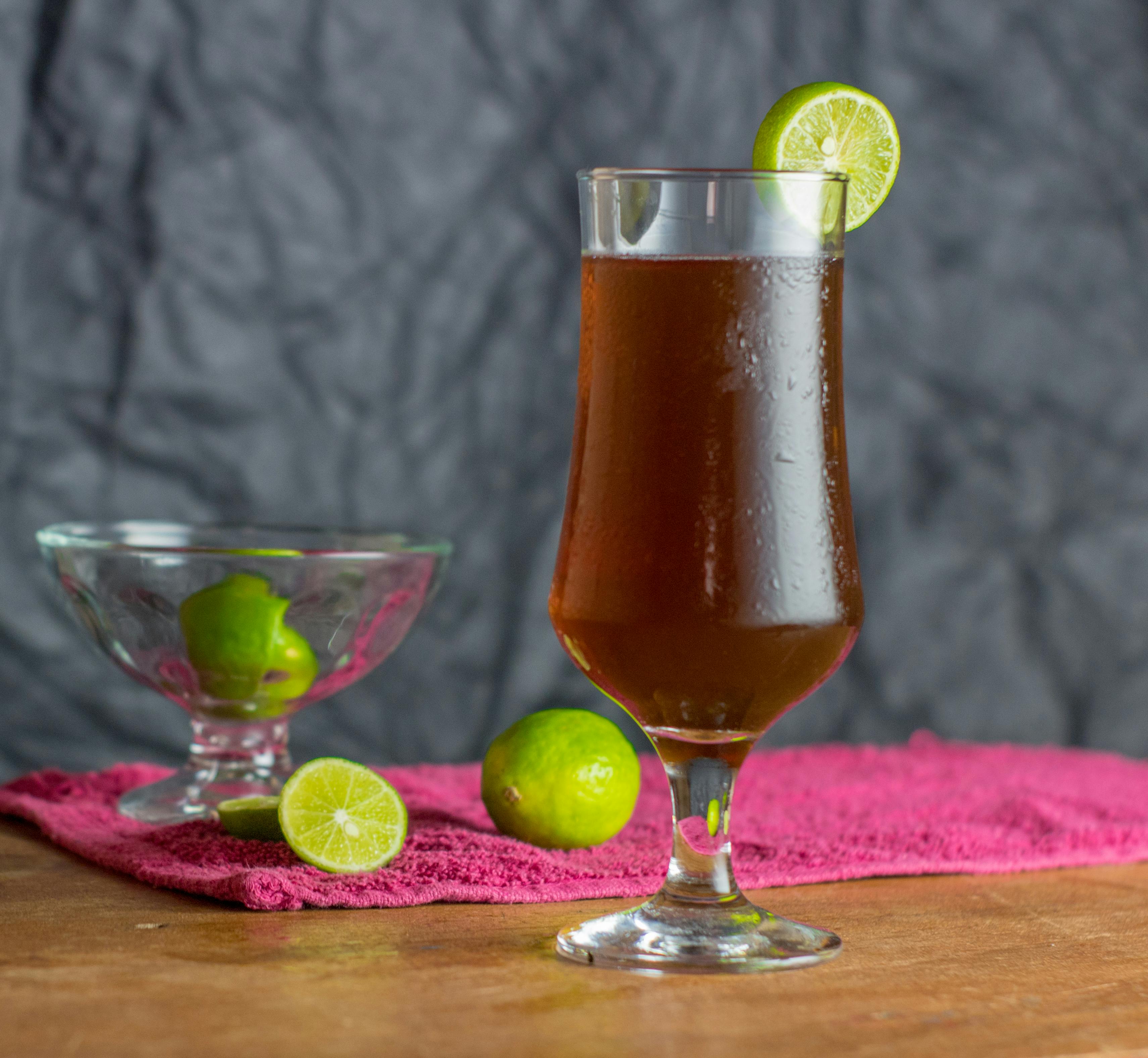 A chilled glass of dark beverage with lime slice, set on a wooden table.