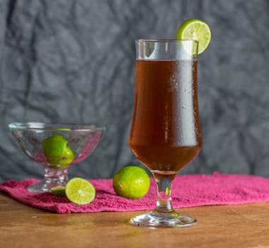 A chilled glass of dark beverage with lime slice, set on a wooden table.