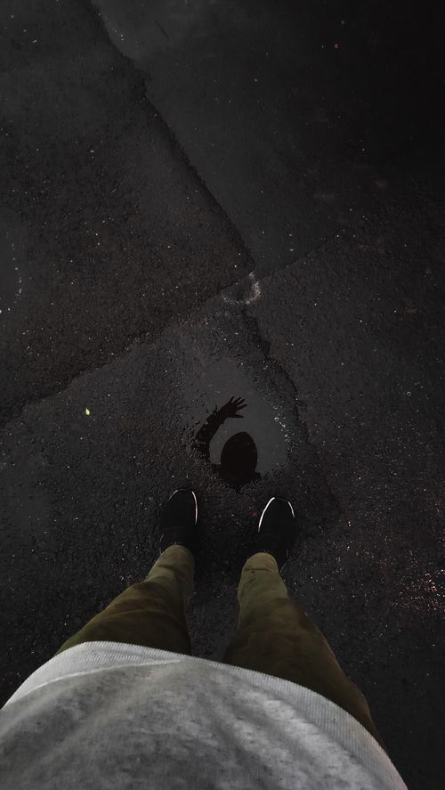 Free Sneakers and brown pants reflected in a puddle on a wet asphalt road, creating a moody atmosphere. Stock Photo