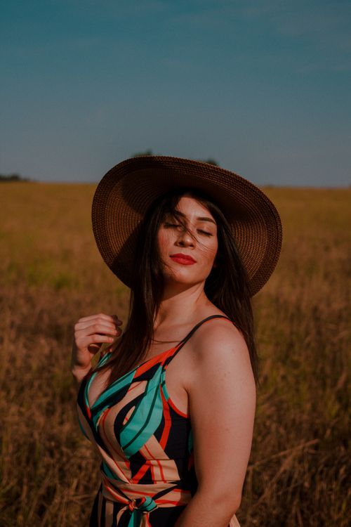 Free A stylish woman with eyes closed poses gracefully in a sunlit field, exuding a sense of elegance and serenity. Stock Photo