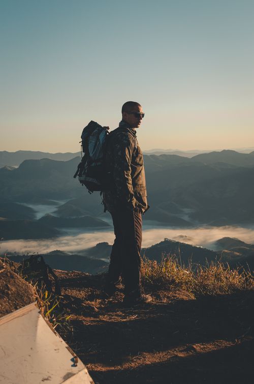 Free A lone hiker with a backpack overlooks a breathtaking mountain landscape at sunrise. Perfect for adventure and travel themes. Stock Photo