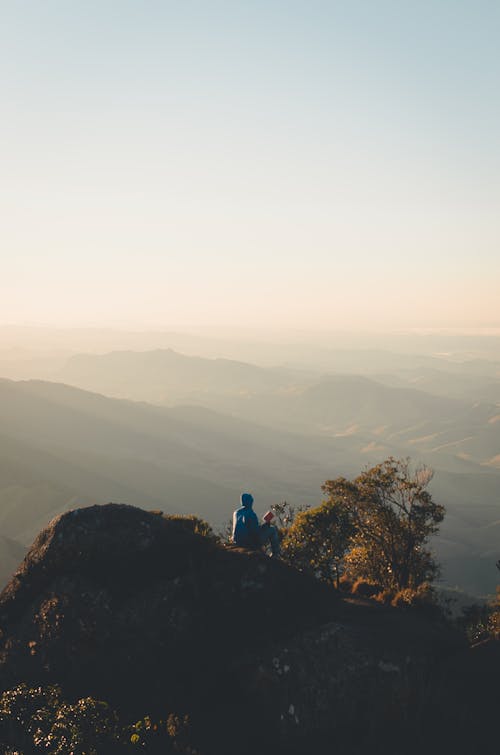 Back View of Person Sitting on Top of Rock Mountain