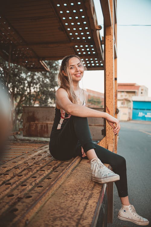 Free Woman in White Tank Top and Black Pants Sitting on Brown Wooden Bench Stock Photo