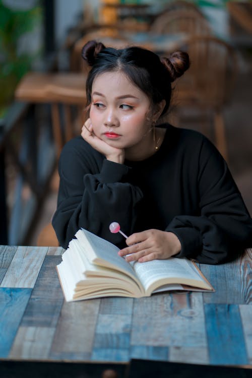 Free Thoughtful young ethnic teen student reading textbook in cafeteria Stock Photo
