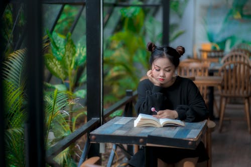 Free Serious young Asian lady reading book in cafeteria Stock Photo