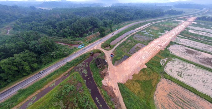 Aerial panorama of a countryside road with lush greenery and farmland in daylight.