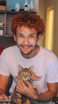一个快乐的卷发男人在室内抱着一只可爱的小猫
