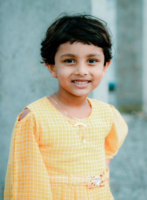 Free Adorable child smiling warmly in a yellow plaid dress, captured in a candid moment outdoors. Stock Photo
