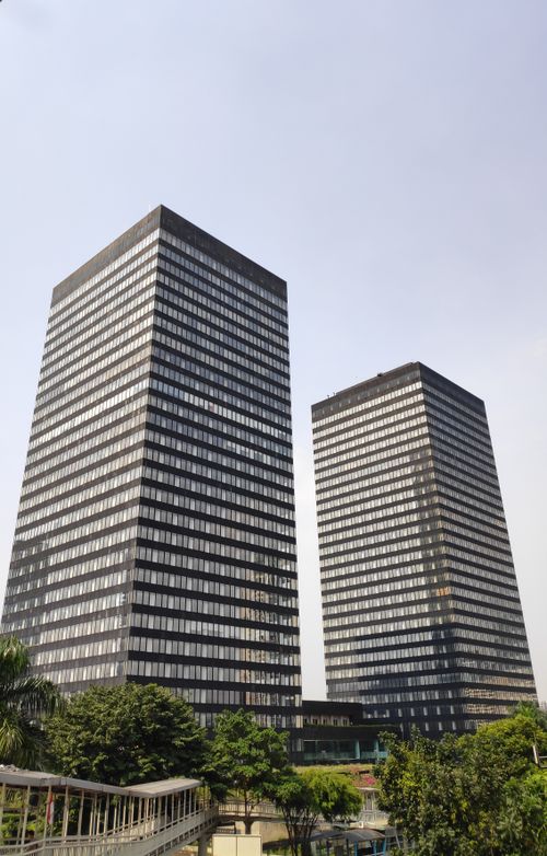 Free View of twin modern skyscrapers in Jakarta, Indonesia, with lush greenery below. Stock Photo