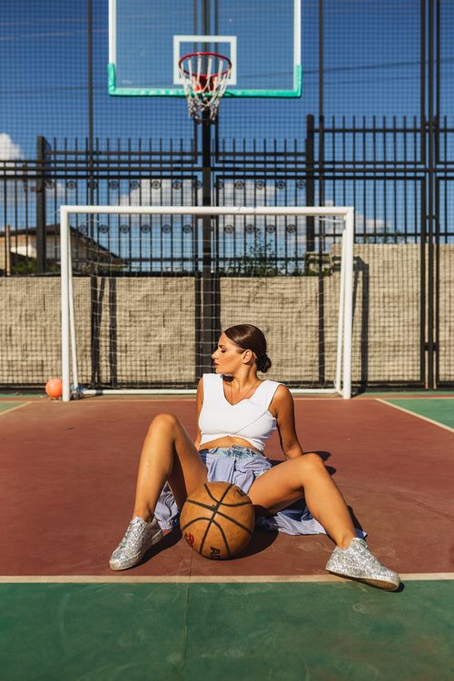 Free Fashionable woman in sporty attire poses with basketball on outdoor court. Stock Photo