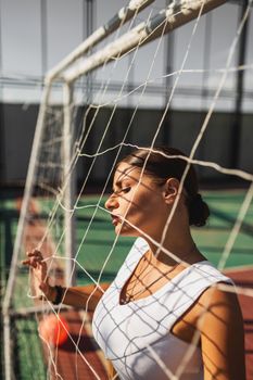 Fashionable woman posing against a soccer net with dramatic lighting and shadows.