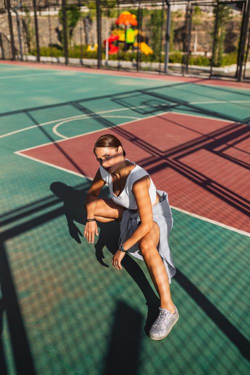 Free Fashionable woman in sunglasses posing on a vibrant basketball court, showcasing edgy style and confidence. Stock Photo
