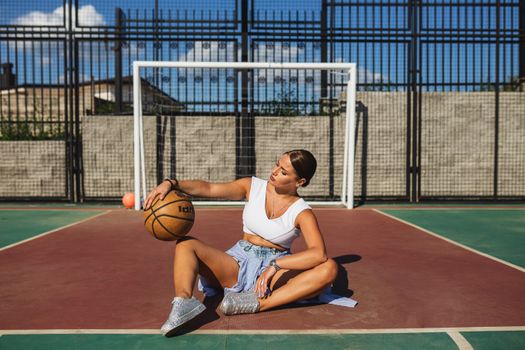 A stylish young woman posing with a basketball on an outdoor court.