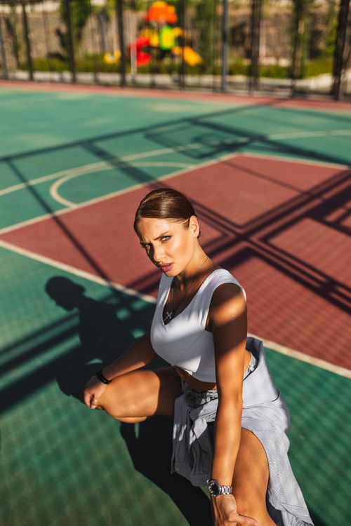 Free Caucasian woman in sporty attire posing on a sunlit outdoor basketball court. Stock Photo