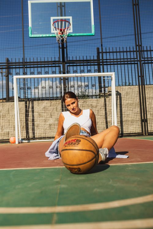 Free Fashionable woman sitting on outdoor basketball court with ball underfoot, exuding style and sportiness. Stock Photo