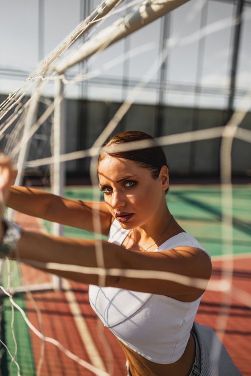 Free Elegant woman in a sporty pose behind a net on a sunny day. Concept of fashion and sports. Stock Photo