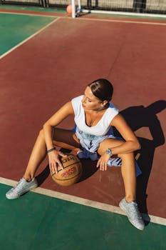 A fashionable young woman poses confidently on an outdoor basketball court during the day.